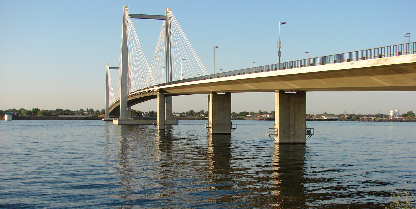 Clearwater Dental | Cable-stayed bridge spanning across a calm river under a clear blue sky, with shoreline vegetation in the foreground.