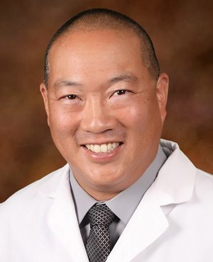 Clearwater Dental | Dr. Jerry C. Han smiling in a white coat with a gray shirt and patterned tie