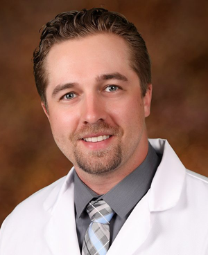 Clearwater Dental | Dr. Eric R. Rose smiling in a white coat with a gray shirt and plaid tie